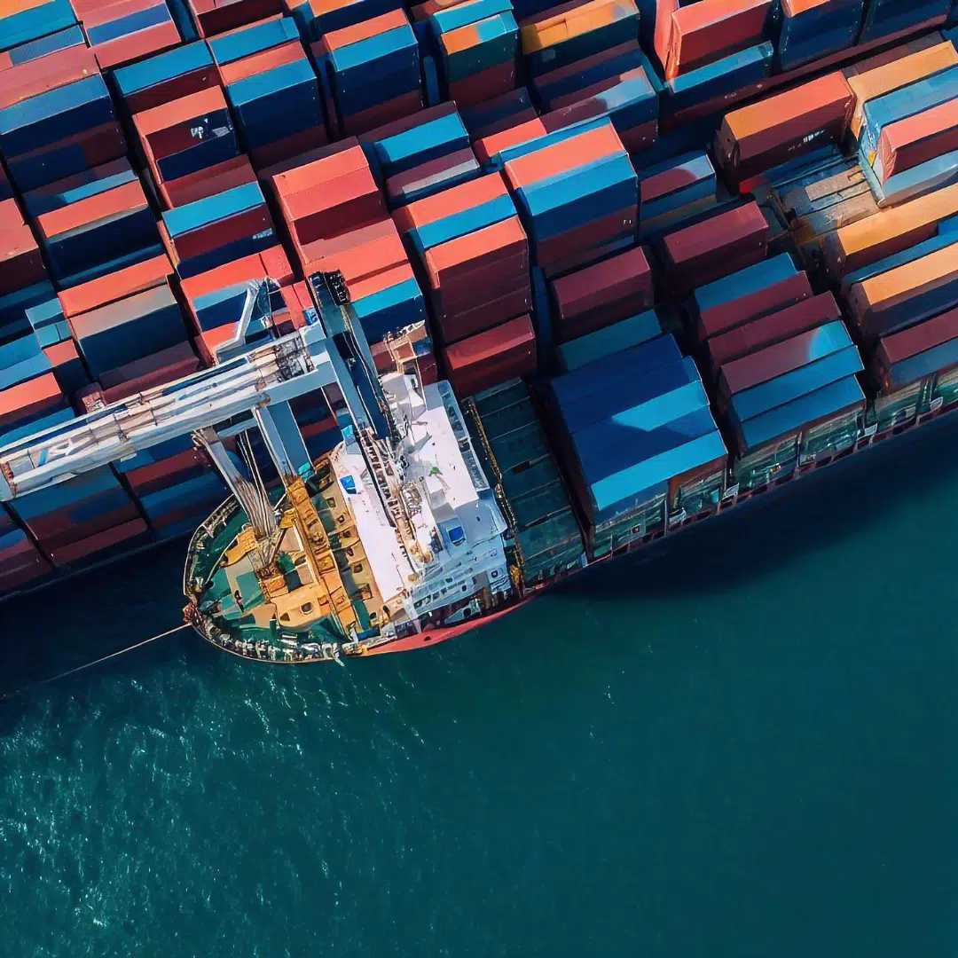 A large container ship, loaded with colorful shipping containers, travels across the blue ocean.